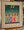 litho from dolf Zwerver Four women dressed in green, blue, pink and white look upward at two bare feet hanging above them, against a blue-green background. framed